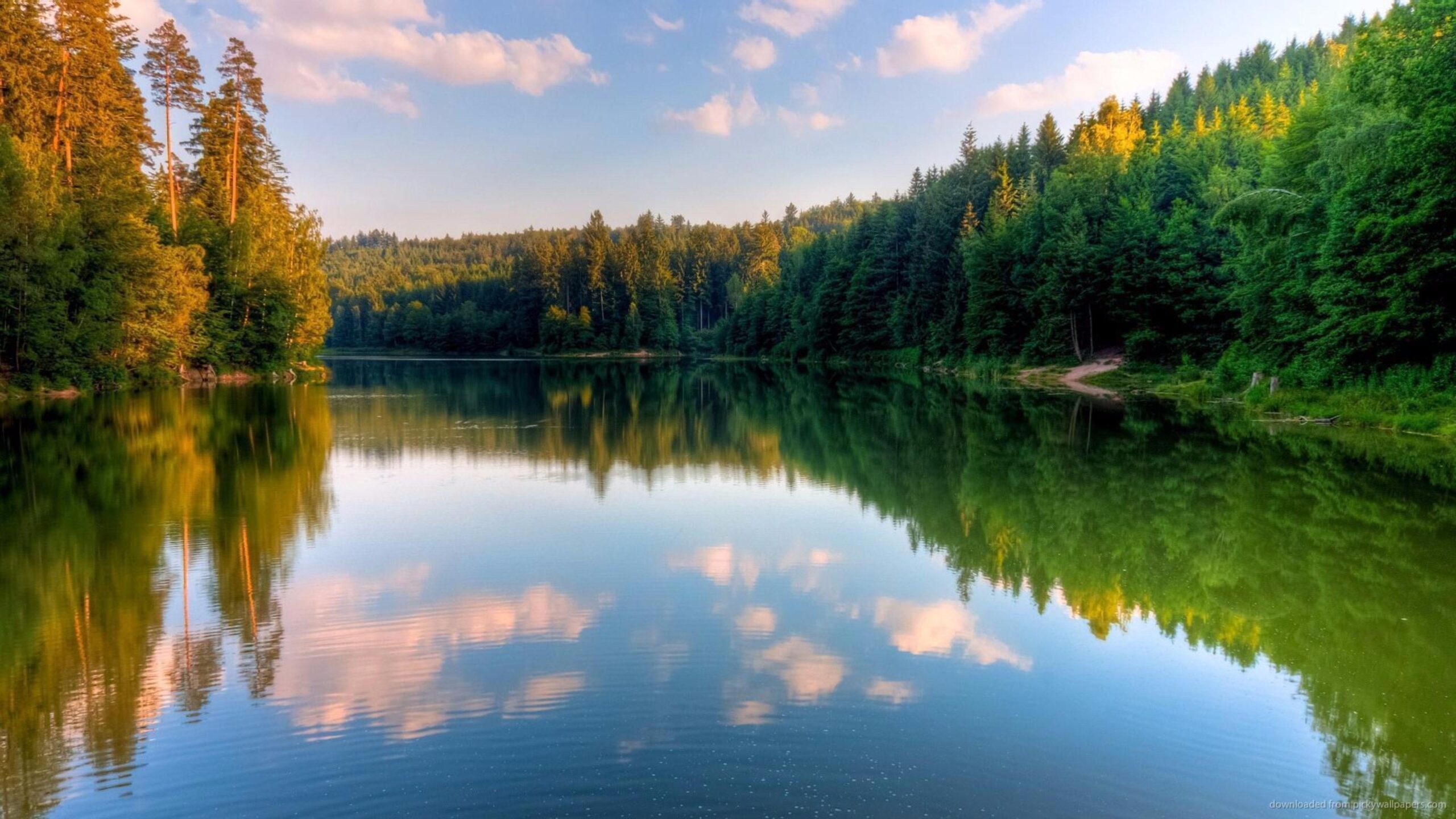 Tranquil lake landscape with mountains and forests in golden sunlight.